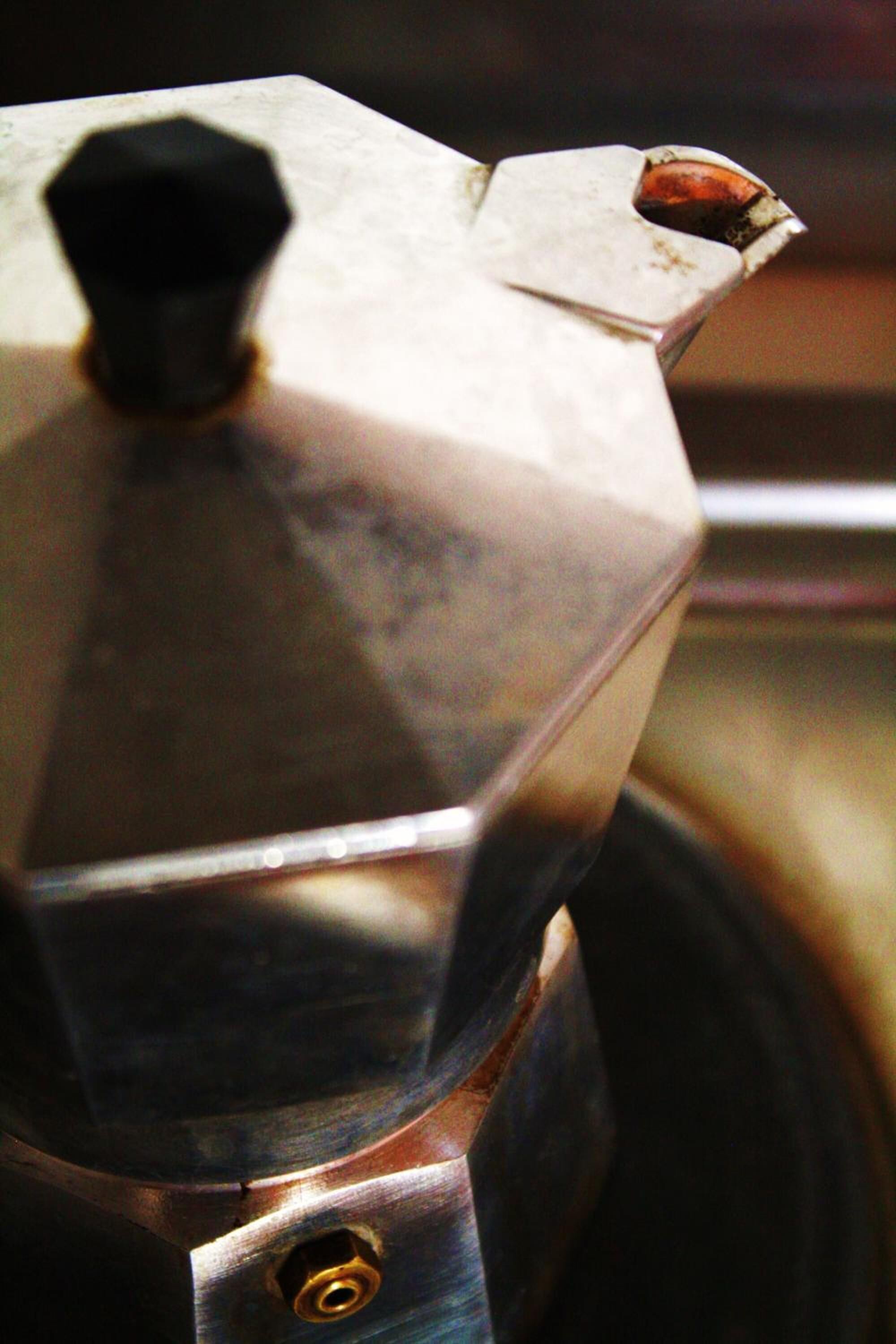 Un primo piano di un oggetto metallico con un pomello e un beccuccio, probabilmente una caffettiera.