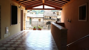 A covered corridor with a checkered floor, a brick wall, and a balcony with potted plants. - Hotel Bed & Wine (Negrar)