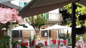 An outdoor dining area with tables covered by red and white checkered tablecloths, white chairs, and a pergola overhead. - Hotel Bed & Wine (Negrar)