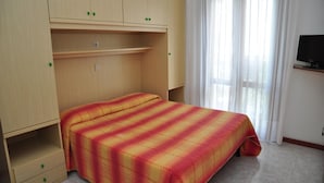 Un dormitorio con cama, armario, televisión y ventana con cortinas.