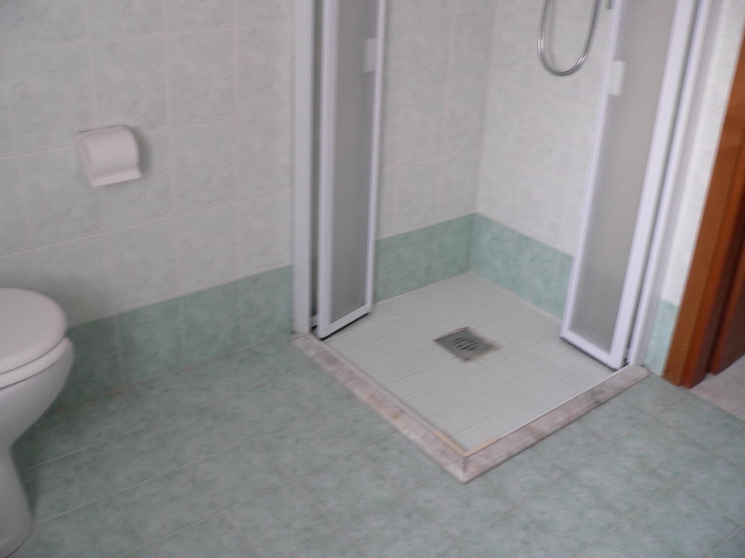 A bathroom with a toilet, a shower with a glass door, and a tiled floor.