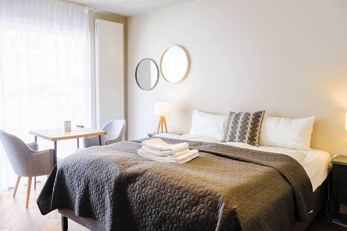 A hotel room with a bed, a desk, a chair, a lamp, and two wall mirrors.