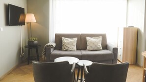 Una sala de estar moderna con un sofá gris, dos sillones, una mesita redonda, una lámpara de pie y un televisor montado en la pared.