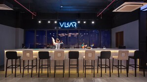 A bar area with a neon sign reading "VBAR", multiple bar stools, and a bartender. - Cross Vibe Viet Tri (Thanh Mieu)