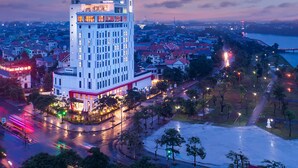 A high-rise hotel with multiple floors, a prominent entrance, and a view of the surrounding cityscape and river. - Cross Vibe Viet Tri (Thanh Mieu)