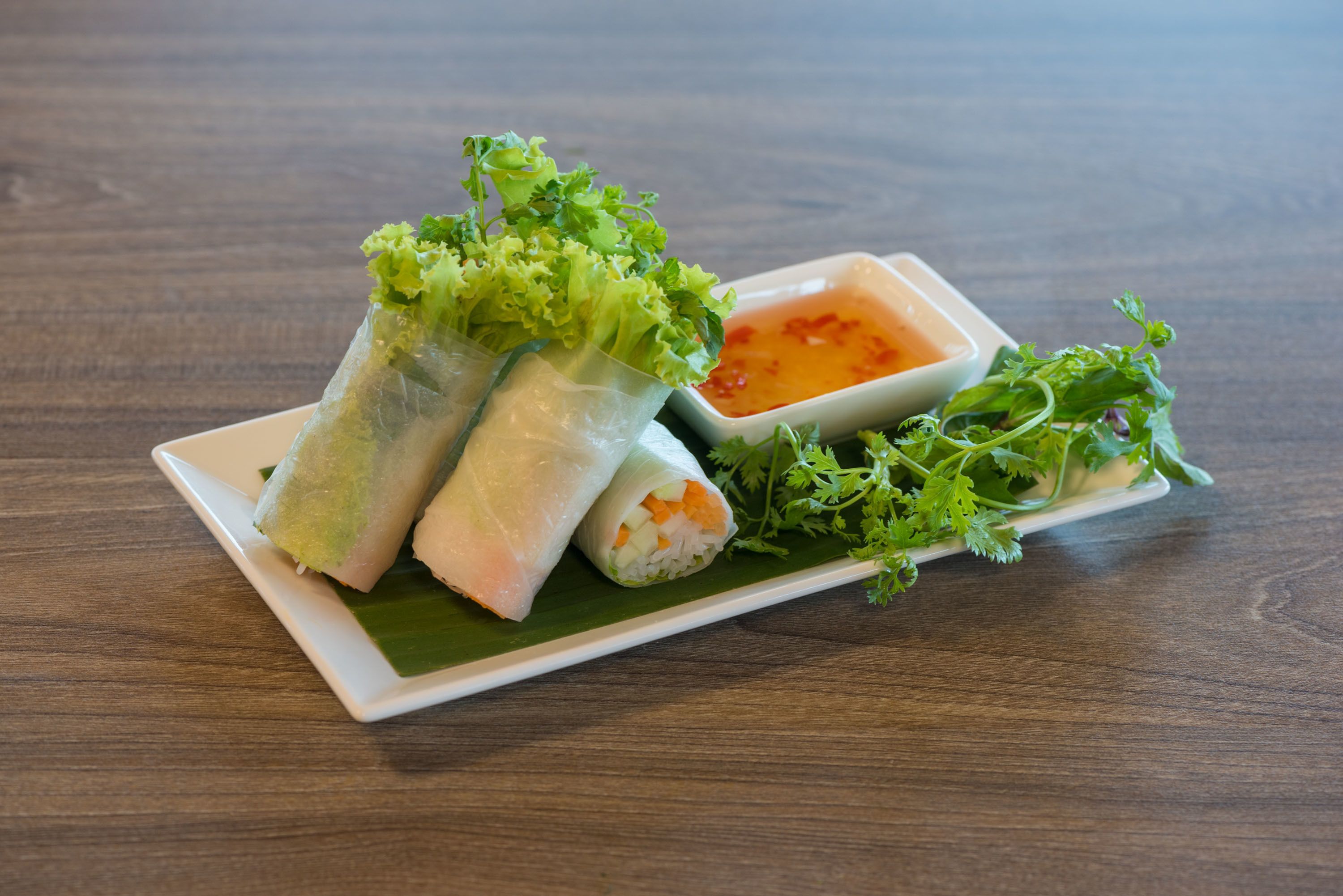 A plate of spring rolls with a side of dipping sauce and fresh herbs.