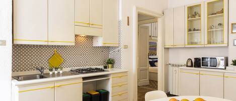 A kitchen with white cabinets, a sink, and a stove. There is a fruit bowl on the table.