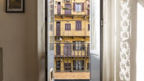 Ein enger Flur mit einer Tür, die auf einen Balkon mit Blick auf ein gelbes Haus mit Fensterläden führt.