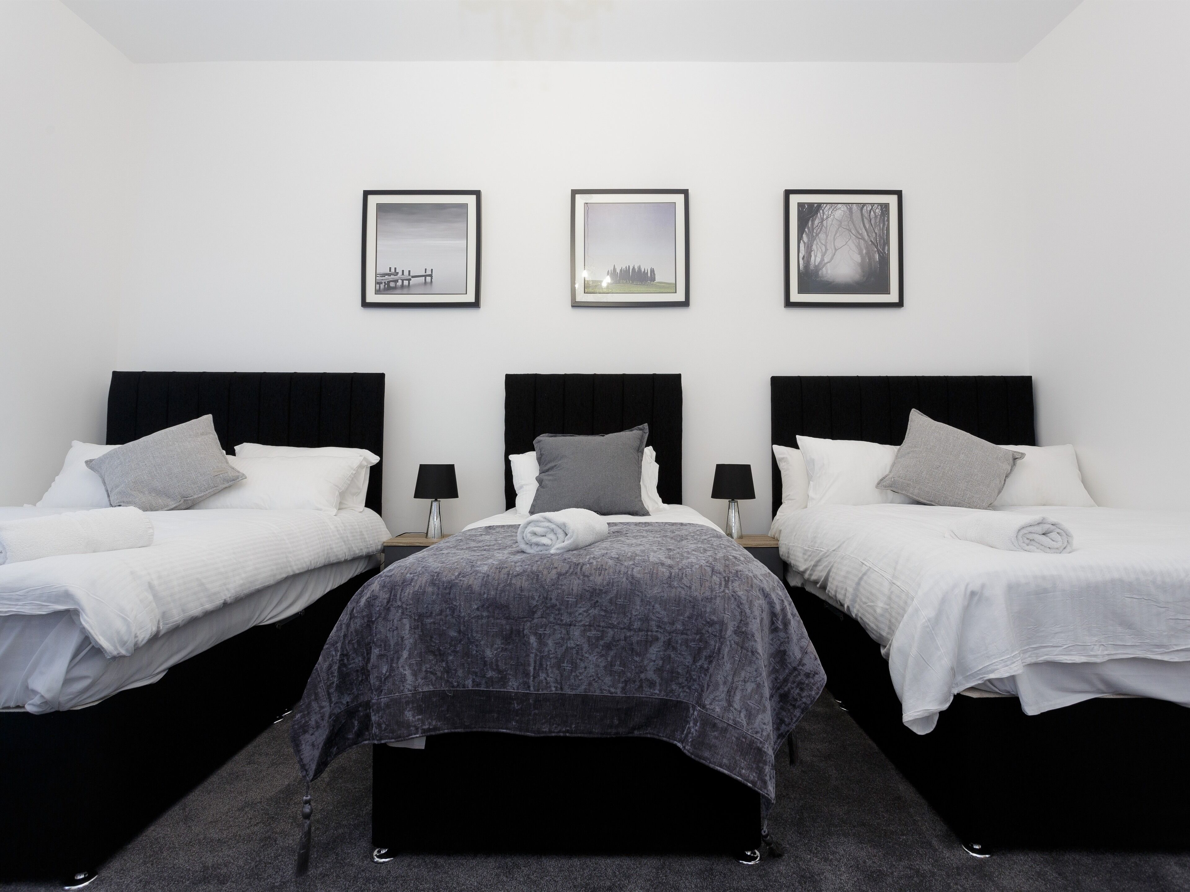 A hotel room with three single beds, a large bed in the center, and three framed pictures on the wall.