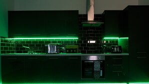 A modern kitchen with black tiles, a stainless steel range hood, and green LED strip lighting. - Live in Leeds Greenhill Bungalows (Leeds)