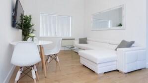 A modern living room with a white sofa, a glass coffee table, and a dining area with a white table and chairs. - Live in Leeds Greenhill Bungalows (Leeds)