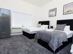 Two single beds with black headboards and white bedding, a wardrobe, and a radiator under the window.