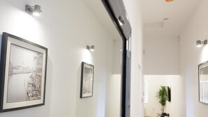 A hallway with framed artwork on the walls, a potted plant, and a television mounted on the wall. - Live in Leeds Greenhill Bungalows (Leeds)