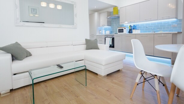 A modern living room with a white sofa, a glass coffee table, and a dining area with white chairs. - Live in Leeds Greenhill Bungalows (Leeds)
