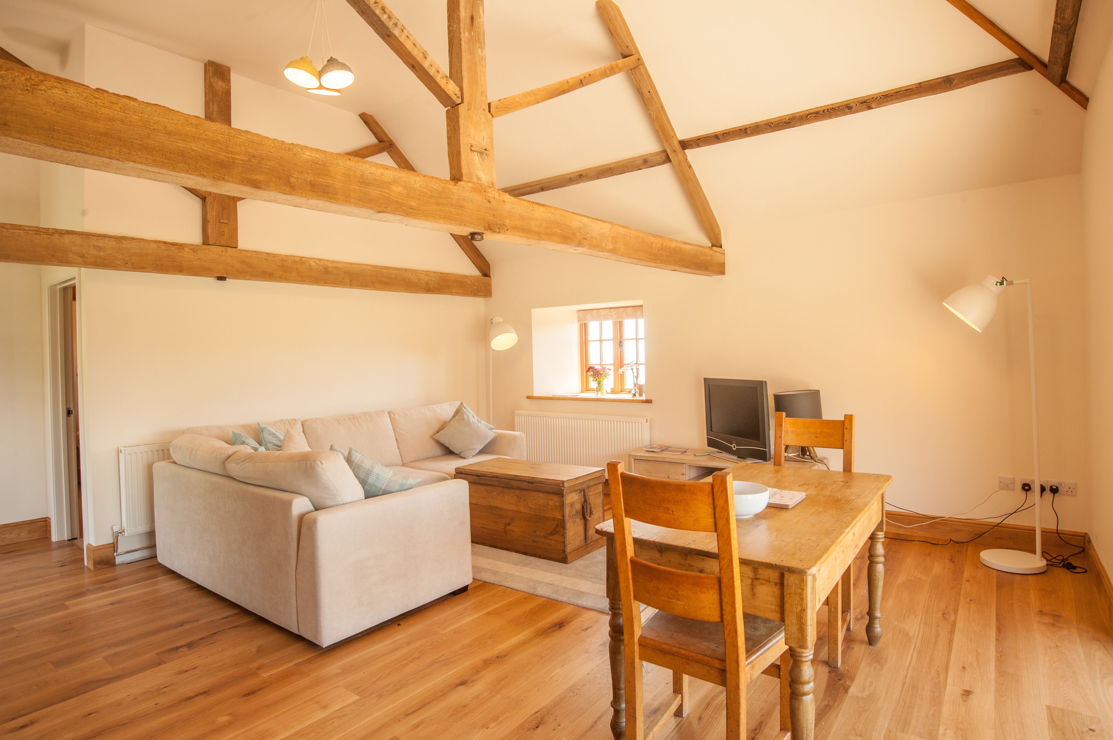 A spacious living room with a wooden ceiling, a sofa, a wooden table, and a TV.