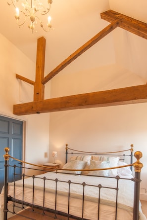 A bedroom with a metal bed frame, wooden beams, a chandelier, and a blue door.