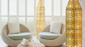 Une pièce comprenant deux fauteuils en osier avec des coussins, un pouf rond et une grande lanterne décorative.