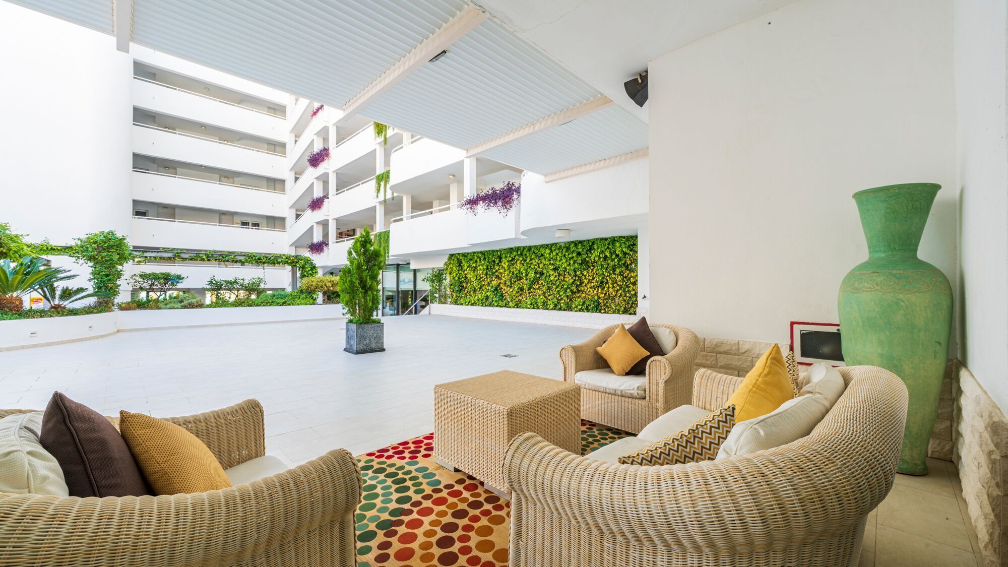 A spacious outdoor area with wicker furniture, a large green vase, and a green wall with plants.