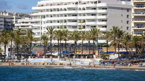 Un hôtel en bord de mer doté de nombreux balcons, de palmiers et de parasols de plage.