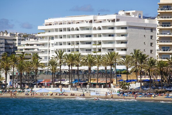 A beachfront hotel with multiple balconies, palm trees, and beach umbrellas. - Hapimag Resort Marbella (Marbella)