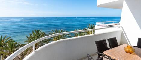 A balcony with a view of the sea, wicker furniture, and a table with a vase.