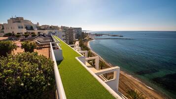 A coastal hotel with a rooftop terrace, a beach view, and a promenade with greenery.