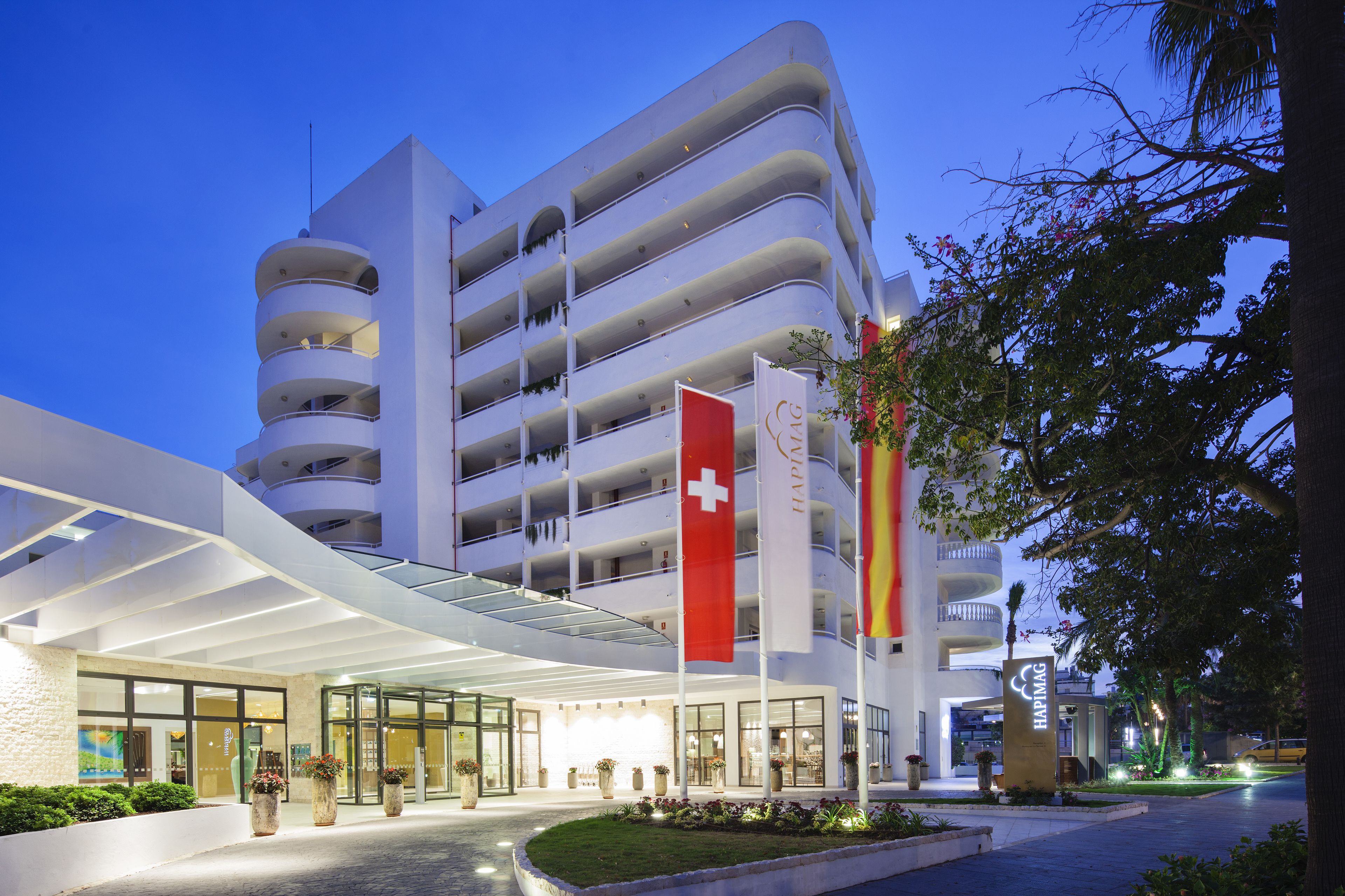 Een meerlaags hotel met een modern ontwerp, met een opvallende Zwitserse vlag en een bord waarop staat dat het een Hapag-Lloyd hotel is.