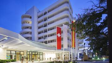 Een meerlaags hotel met een modern ontwerp, met een opvallende Zwitserse vlag en een bord waarop staat dat het een Hapag-Lloyd hotel is.