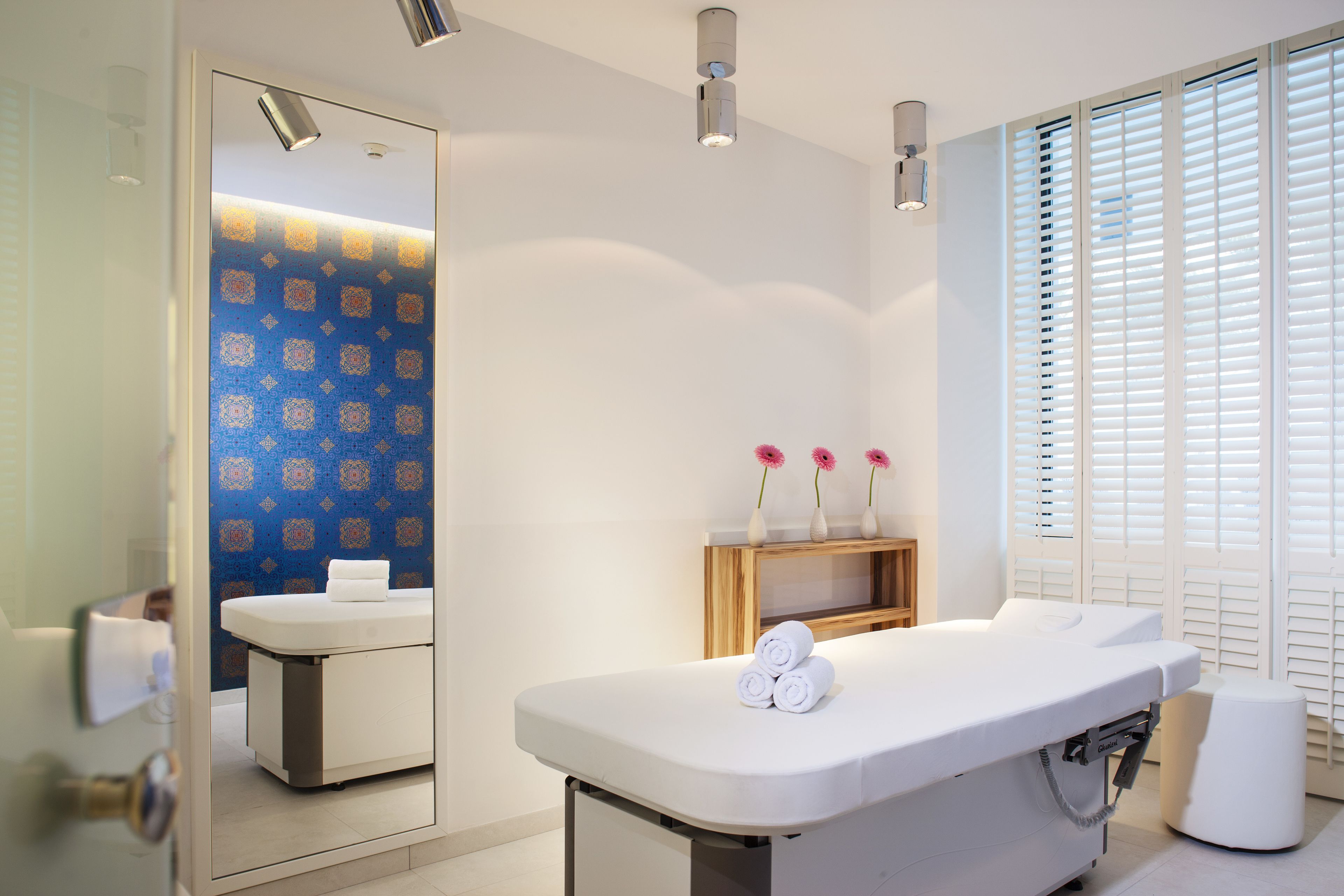 A modern bathroom with a large mirror, a white countertop, and a wooden shelf with decorative items.