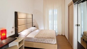 Ein Hotelzimmer mit Bett, Schreibtisch mit Lampe, Fernseher und einem Fenster mit Vorhängen.