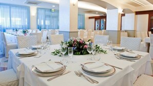 Ein Festsaal mit runden Tischen, gedeckt für eine festliche Veranstaltung, mit weißen Tischdecken, goldfarbenen Tellern und floralen Mittelpunkten.