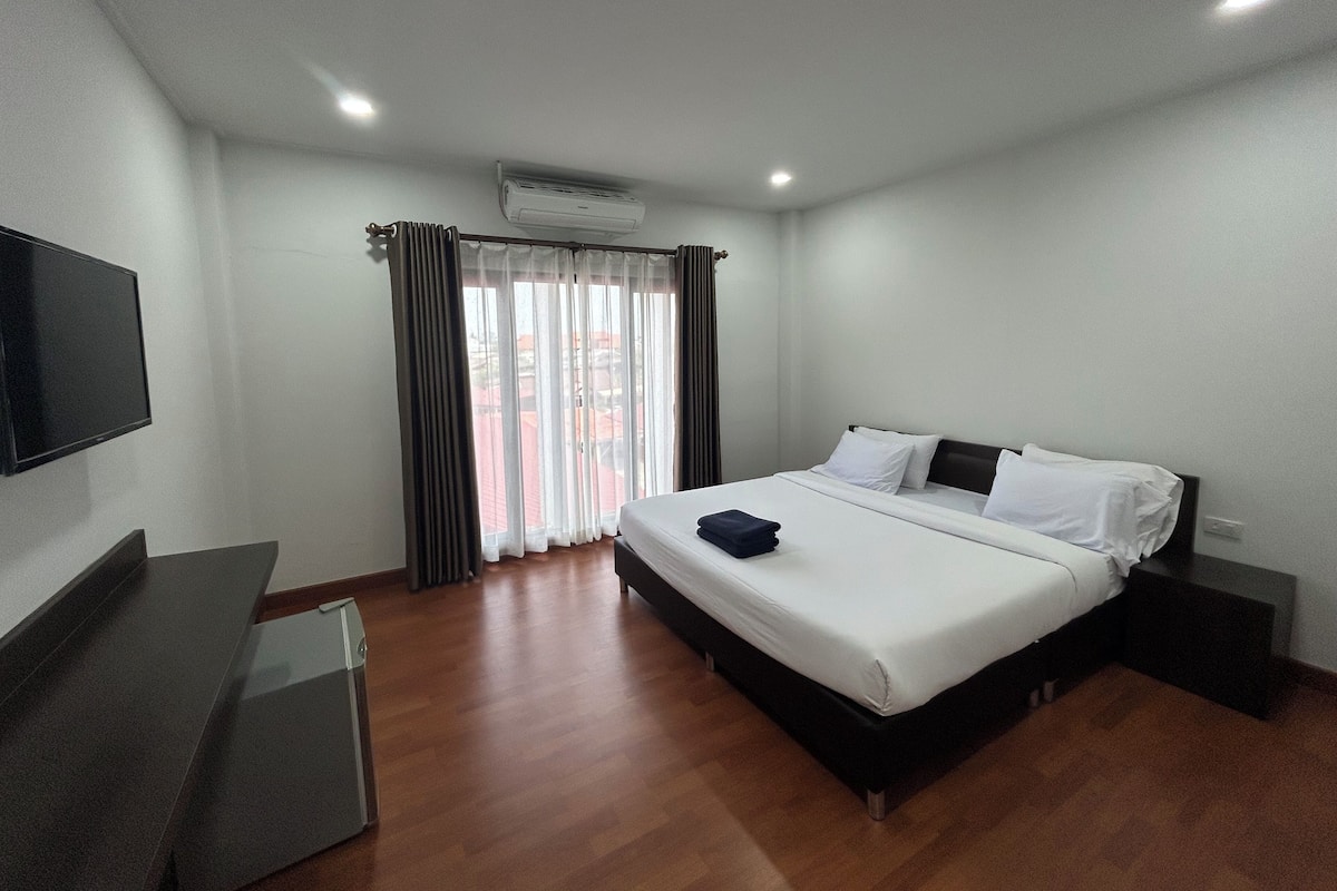 A modern hotel room with a large bed, a flat-screen TV, and a window with curtains.