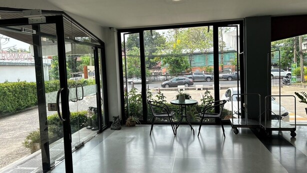 A modern interior with large windows, a seating area with chairs and a table, and a view of the street outside. - Bordin Hotel (Ubon Ratchathani)