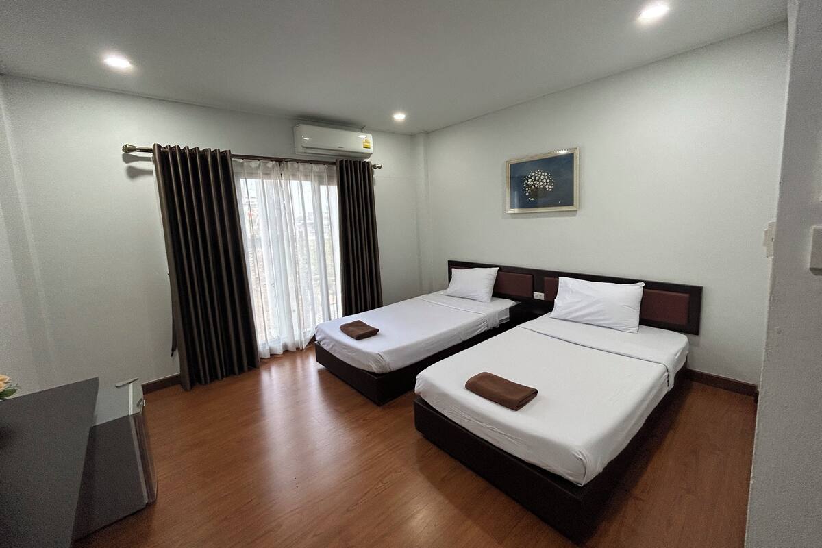 A hotel room with two single beds, a desk, and a window with curtains.