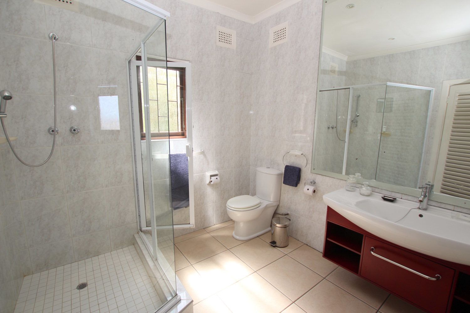 Un baño con cabina de ducha de vidrio, inodoro, lavabo con espejo y ventana.