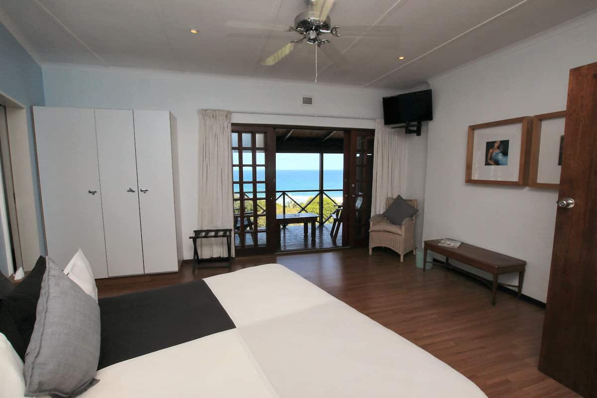 A bedroom with a large bed, a chair, a table, and a view of the ocean through a door.