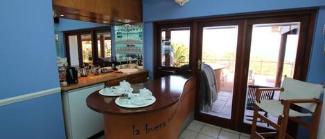 A kitchen with a bar area, a counter with teapots, and a view of the outdoors.