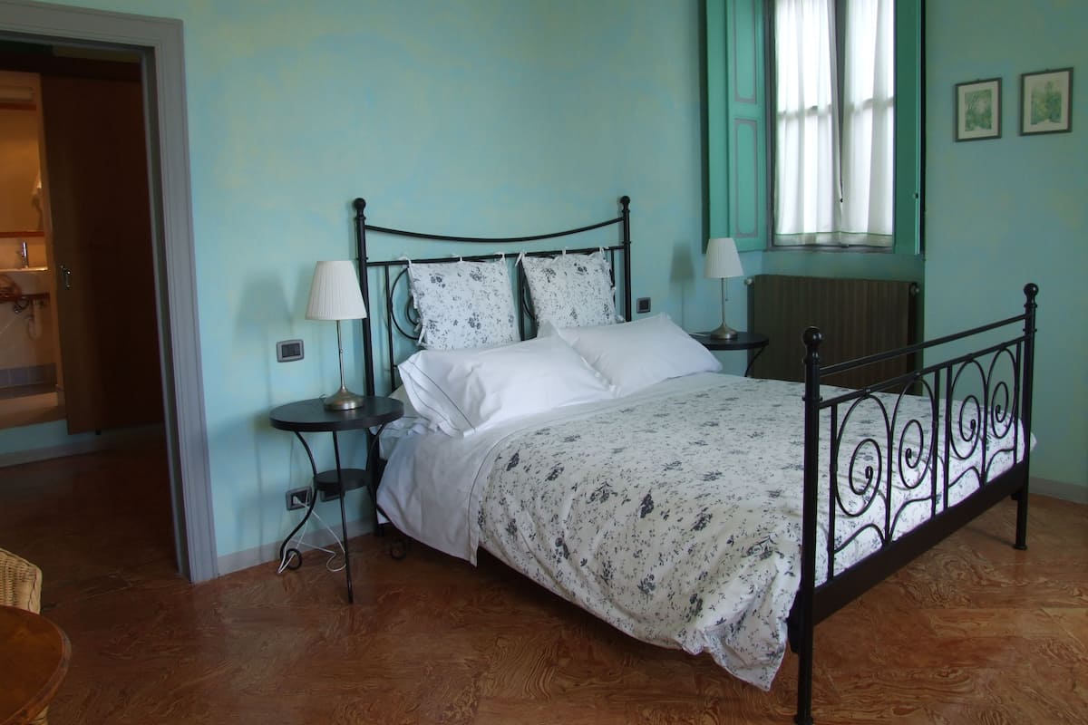 A bedroom with a bed, two bedside tables, a window with curtains, and a door.