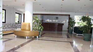 Un hall con mostrador de recepción, una zona de estar con un sillón redondo y varias plantas en macetas.