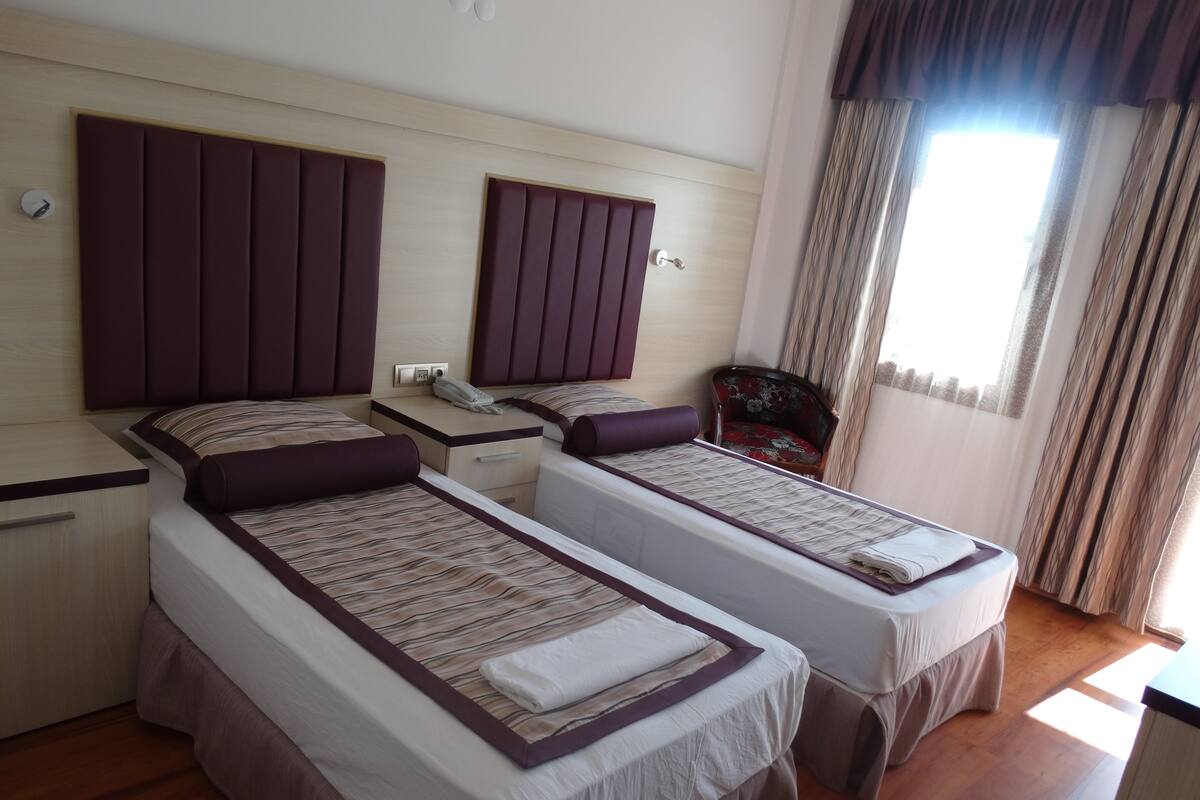 Quarto de hotel com duas camas de solteiro, uma mesa de cabeceira de madeira com telefone e uma cadeira.