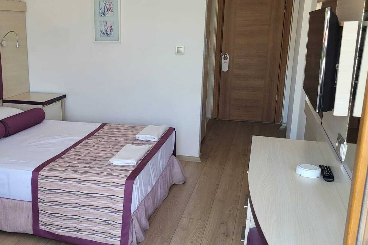 Quarto com cama, mesas de cabeceira, telefone, porta e uma obra de arte na parede.