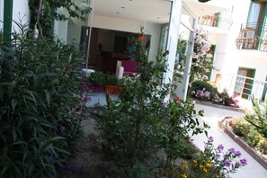 Ein Innenhof mit Kübelpflanzen und Blumen, eine Sitzgruppe mit Tisch und Stühlen sowie ein Gebäude mit Balkonen.