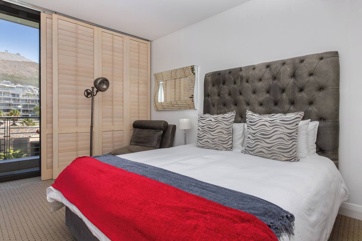 Une chambre d’hôtel avec un grand lit, une vue par une porte coulissante, une lampe sur pied et un miroir au mur.