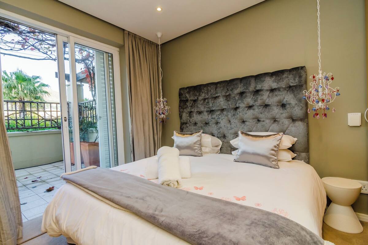 Ein Schlafzimmer mit einem großen Bett, einem mit Wirbeln verzierten Kopfteil, einer Chandelüster und Blick ins Freie durch eine Schiebetür.