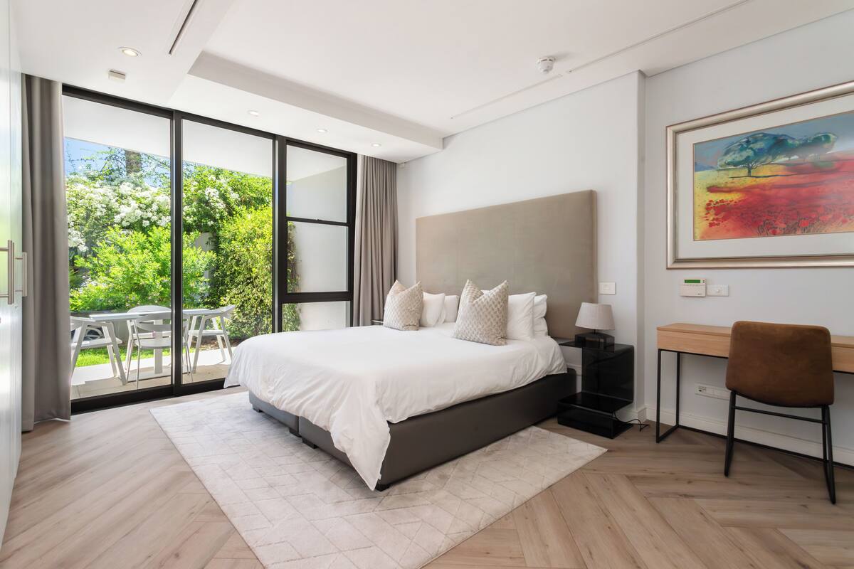 Une chambre moderne avec un grand lit, un bureau et une vue sur la verdure grâce à la porte-fenêtre coulissante.