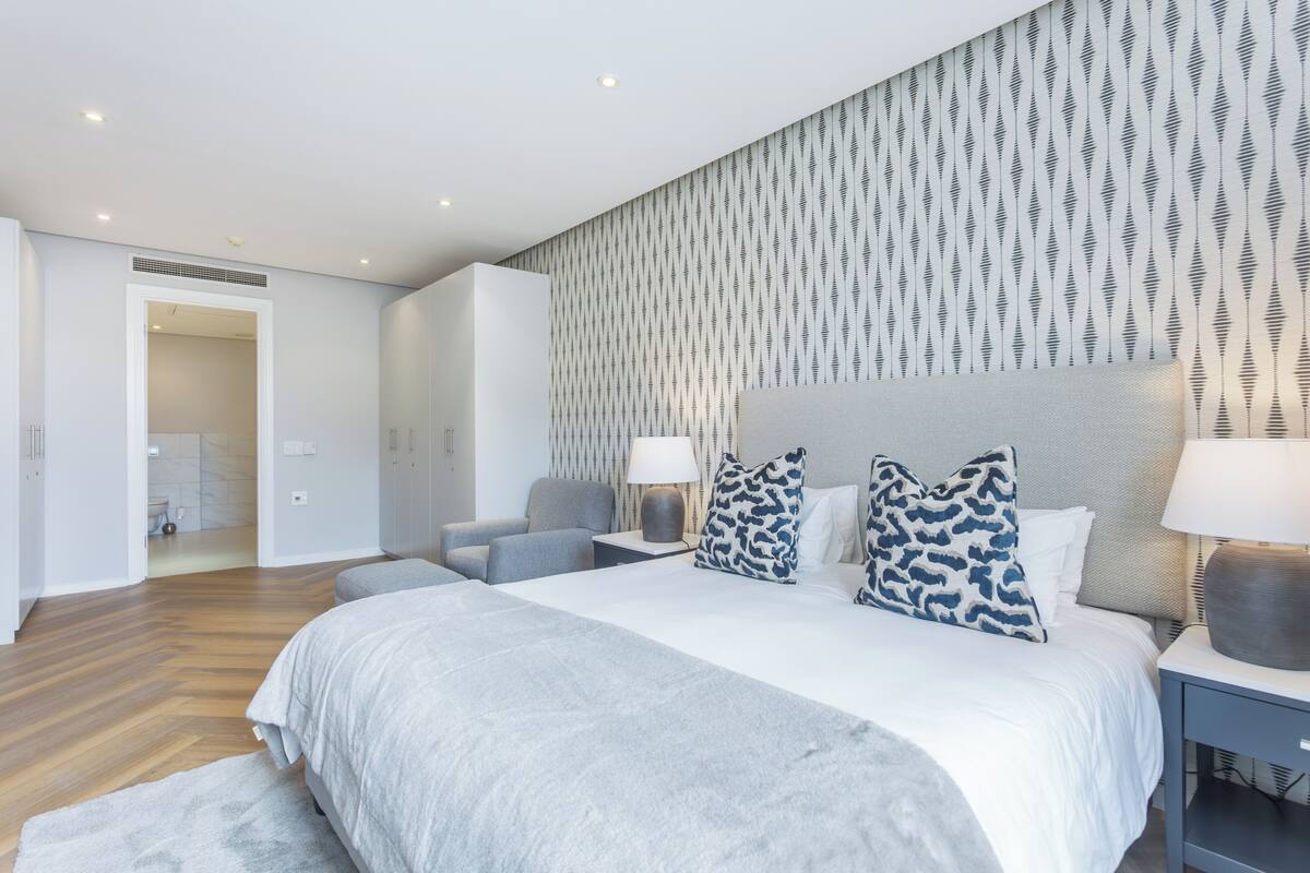 Ein modernes Schlafzimmer mit einem großen Bett, einem Nachttisch, einem Sessel und einer Wand mit Muster.