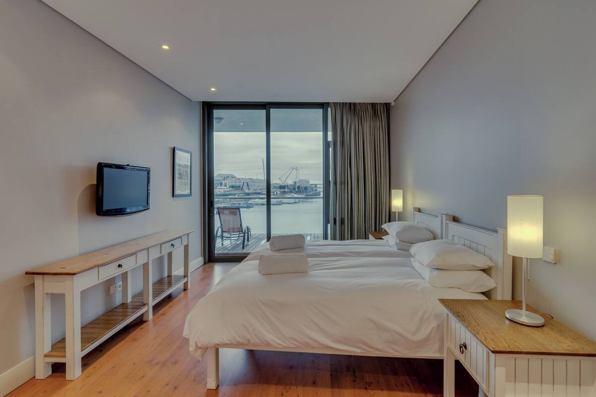 Une chambre d’hôtel moderne dotée d’un grand lit, d’un téléviseur fixé au mur, d’un balcon offrant une vue sur la ville et d’une console en bois.