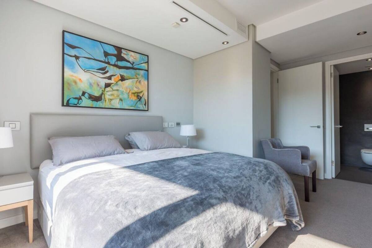 Ein modernes Schlafzimmer mit einem großen Bett, einem Sessel, einem Gemälde und einem durchgegangenen Tür angedeuteten Badezimmer.