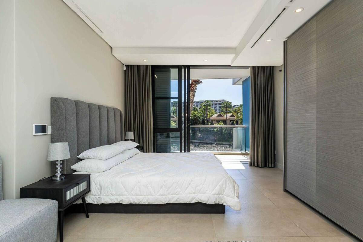 Une chambre moderne avec un grand lit, une table de chevet, une lampe et une vue sur l’extérieur grâce à une porte-fenêtre coulissante.