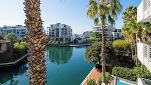 A waterfront hotel with modern architecture, a canal, and palm trees. - Mountain Marina Luxury Apartments (Cape Town)